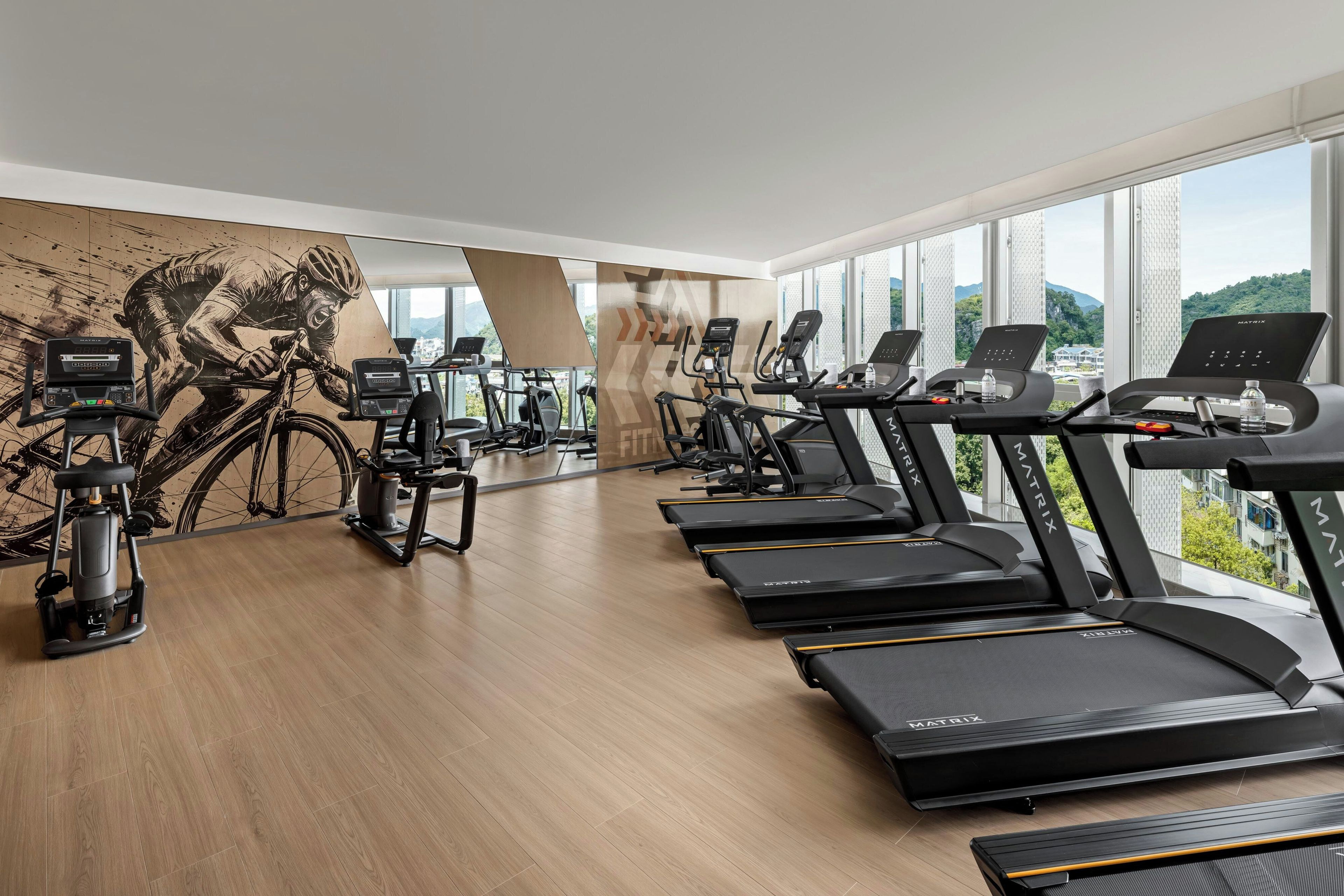 Een sportschool met meerdere loopbanden, hometrainers en een roeiapparaat.