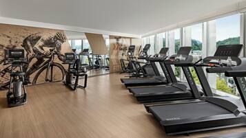 Een sportschool met meerdere loopbanden, hometrainers en een roeiapparaat.