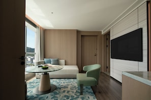 Habitación de hotel moderna con un televisor grande, un sofá, una mesa redonda y vistas a la ciudad.