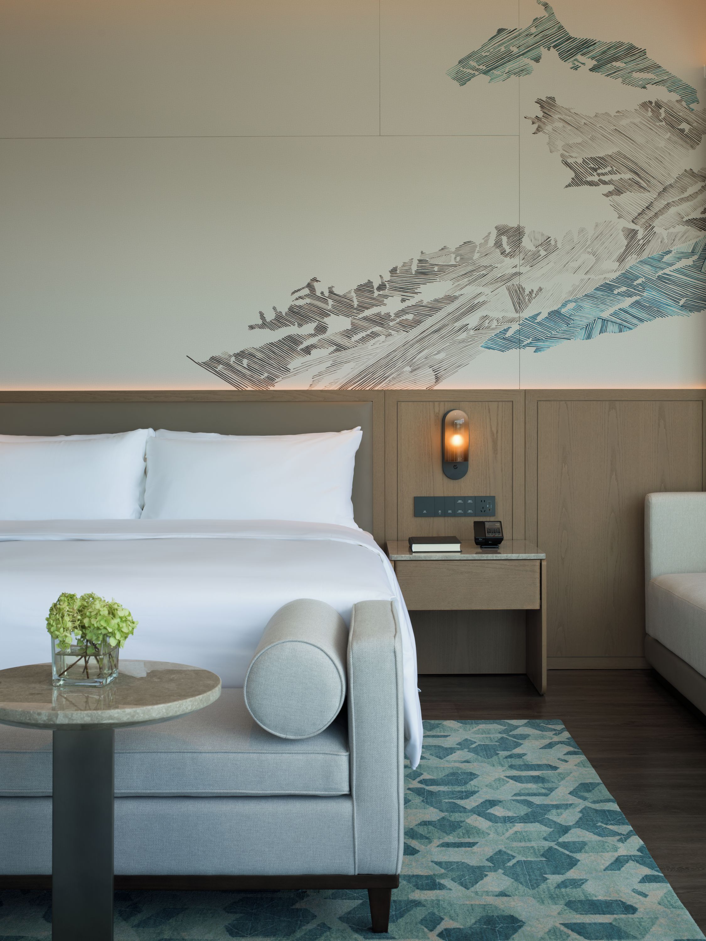 Una habitación de hotel moderna con una cama grande, una mesita de noche con lámpara y un mural decorativo en la pared.