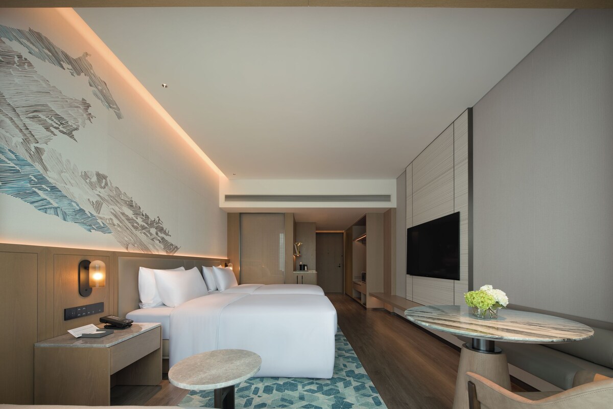 A modern hotel room with a bed, bedside table, lamp, and a flat-screen TV.