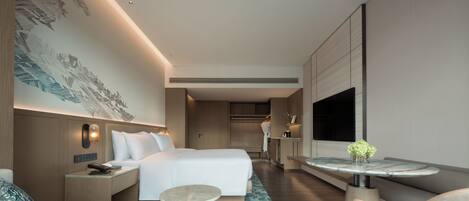 A modern hotel room with a bed, bedside table, lamp, and a small round table with a vase of flowers.