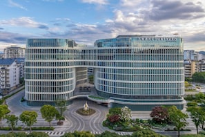 Un hotel moderno con fachada de vidrio curva, un patio central con fuente y vistas a la ciudad circundante.