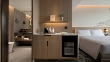 A modern hotel room with a bed, a minibar, a bathroom, and a view of a mountain.