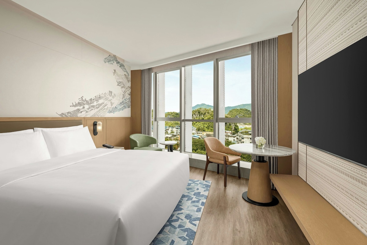 Quarto de hotel com uma cama grande, escrivaninha, cadeira e vista da cidade.