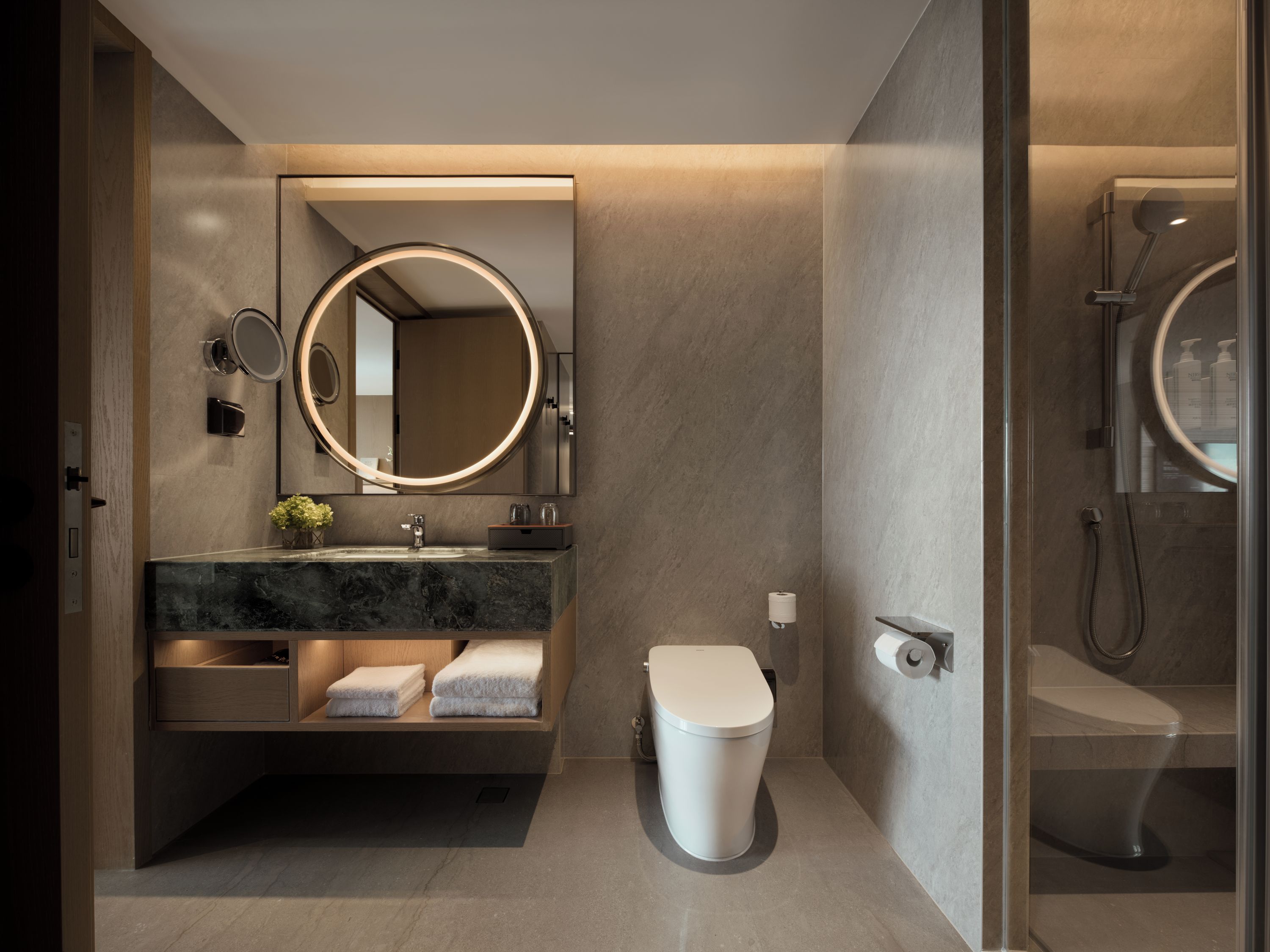 A modern bathroom with a marble vanity, a toilet, and a glass-enclosed shower area.