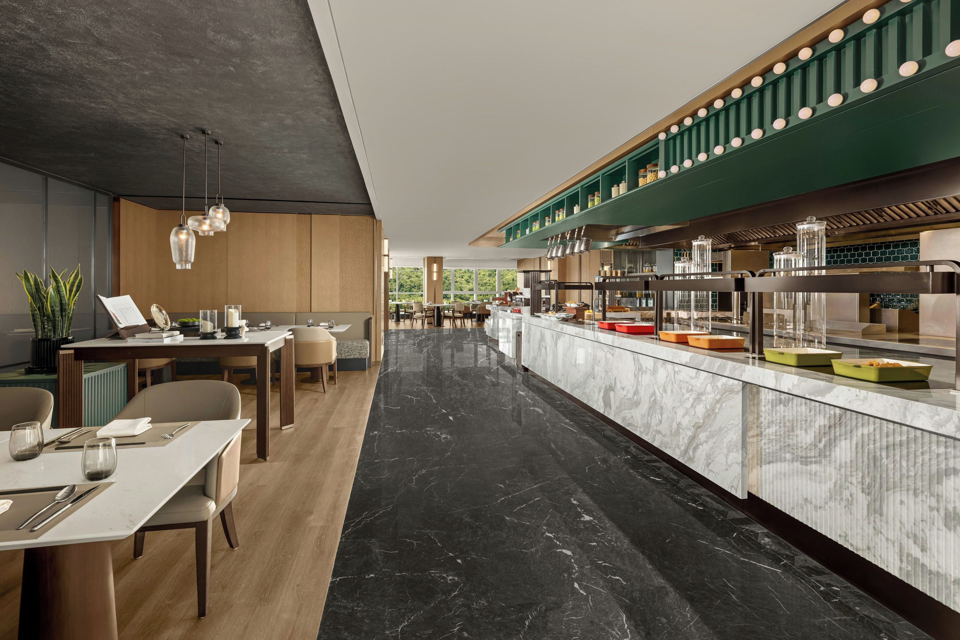 Un restaurant moderne doté d’un sol en marbre, de meubles en bois et d’un mur d’accent de couleur verte.