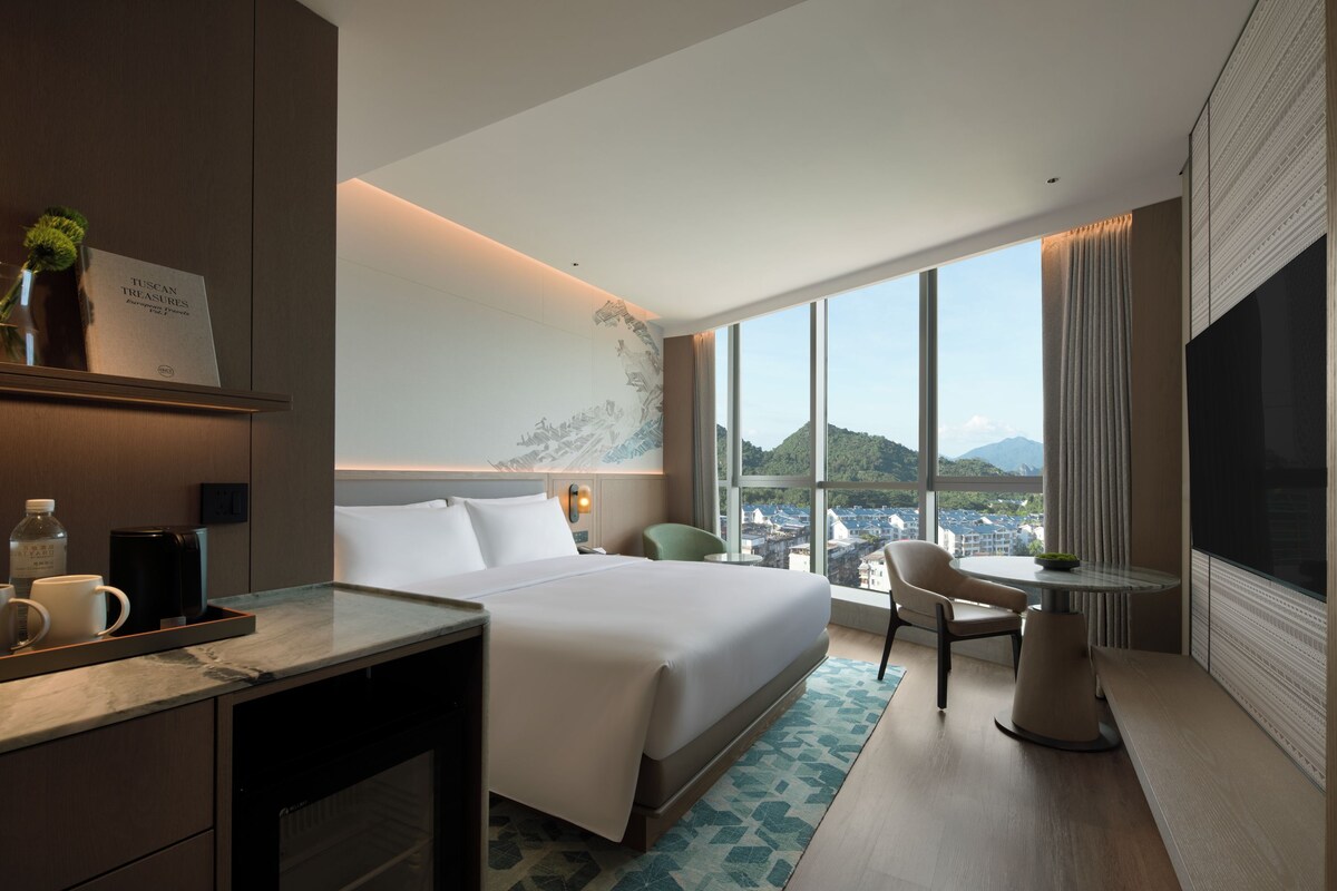 A hotel room with a large bed, a desk with a coffee maker, a chair, and a TV.