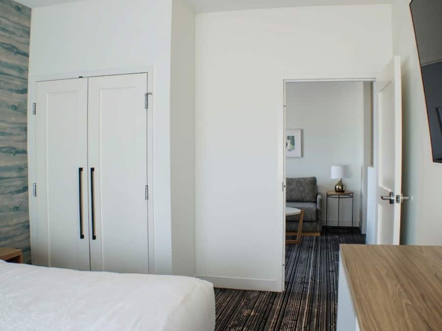A hotel room with a bed, wardrobe, and a small seating area with a sofa and table.