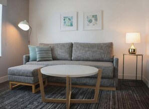 Una sala de estar moderna con un sofá gris, una mesa redonda y dos lámparas de pared.