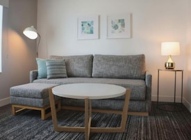 A modern living room with a grey sofa, a round table, and two wall-mounted lamps.