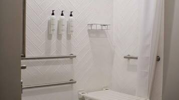 A walk-in shower with a white tiled wall, a showerhead, a towel rack, and a shelf with toiletries.