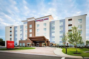 A Towneplace Suites Marriott hotel with a modern design, featuring a central entrance, multiple floors, and a landscaped outdoor area with seating.