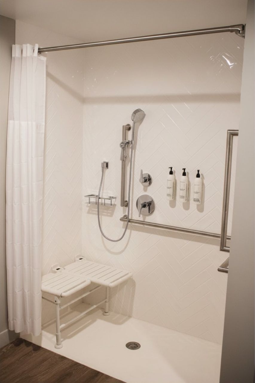 Ducha con cabezal de ducha de mano, puerta de vidrio y un pequeño estante con artículos de aseo.