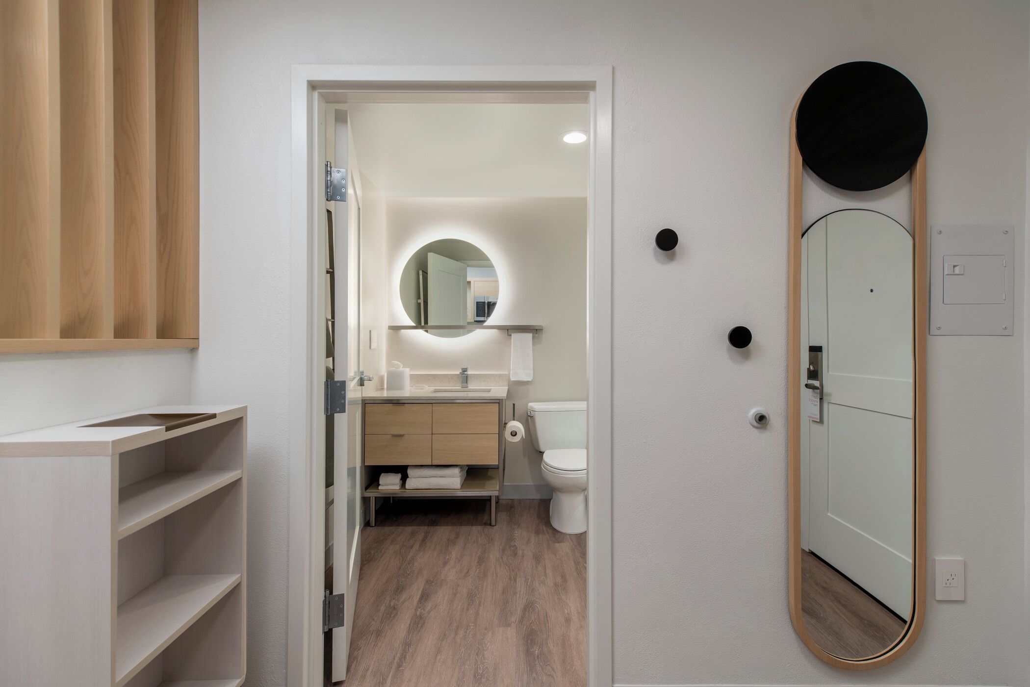 A modern bathroom with a wooden vanity, a round mirror, and a toilet.