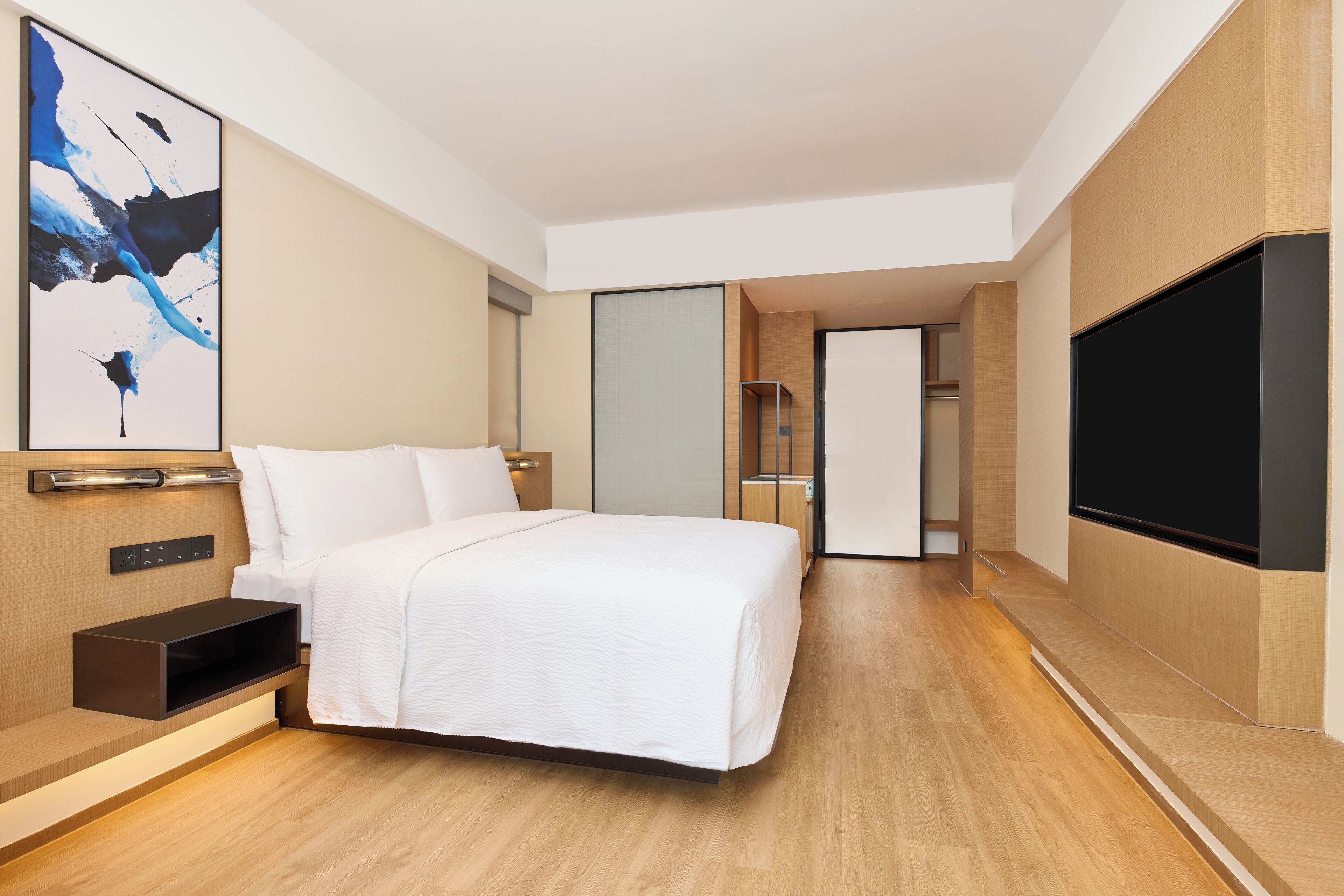 Habitación de hotel moderna con una cama grande, un televisor de pantalla plana, un cuadro en la pared y piso de madera.