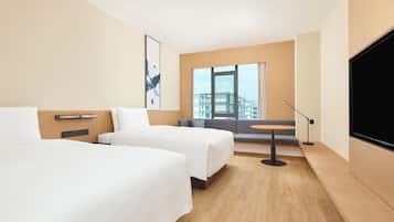 A hotel room with two beds, a sofa, a small table, a TV, and a window with a view of buildings.