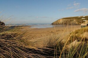 Une plage avec une zone herbeuse au premier plan, une rive sablonneuse et une falaise rocheuse en arrière-plan.
