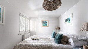 Ein Schlafzimmer mit einem großen Bett, einem Nachttisch, einer Lampe und einem Korbstuhl.