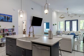 A modern kitchen with a central island, a dining area with a blue accent wall, and a living room with a large window. - Hot Tub+Game Room+Pet-Friendly+Lake Access+FirePit (Mabank)