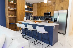Eine moderne Küche mit Holzausbau, einer zentralen Kochinsel mit Barhocker, Edelstahlgeräten und einer Küchenwand mit Fischgrätmuster-Fliesen.