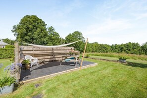 Eine Holzterrasse mit Bank und Picknicktisch, umgeben von Rasen und Bäumen.