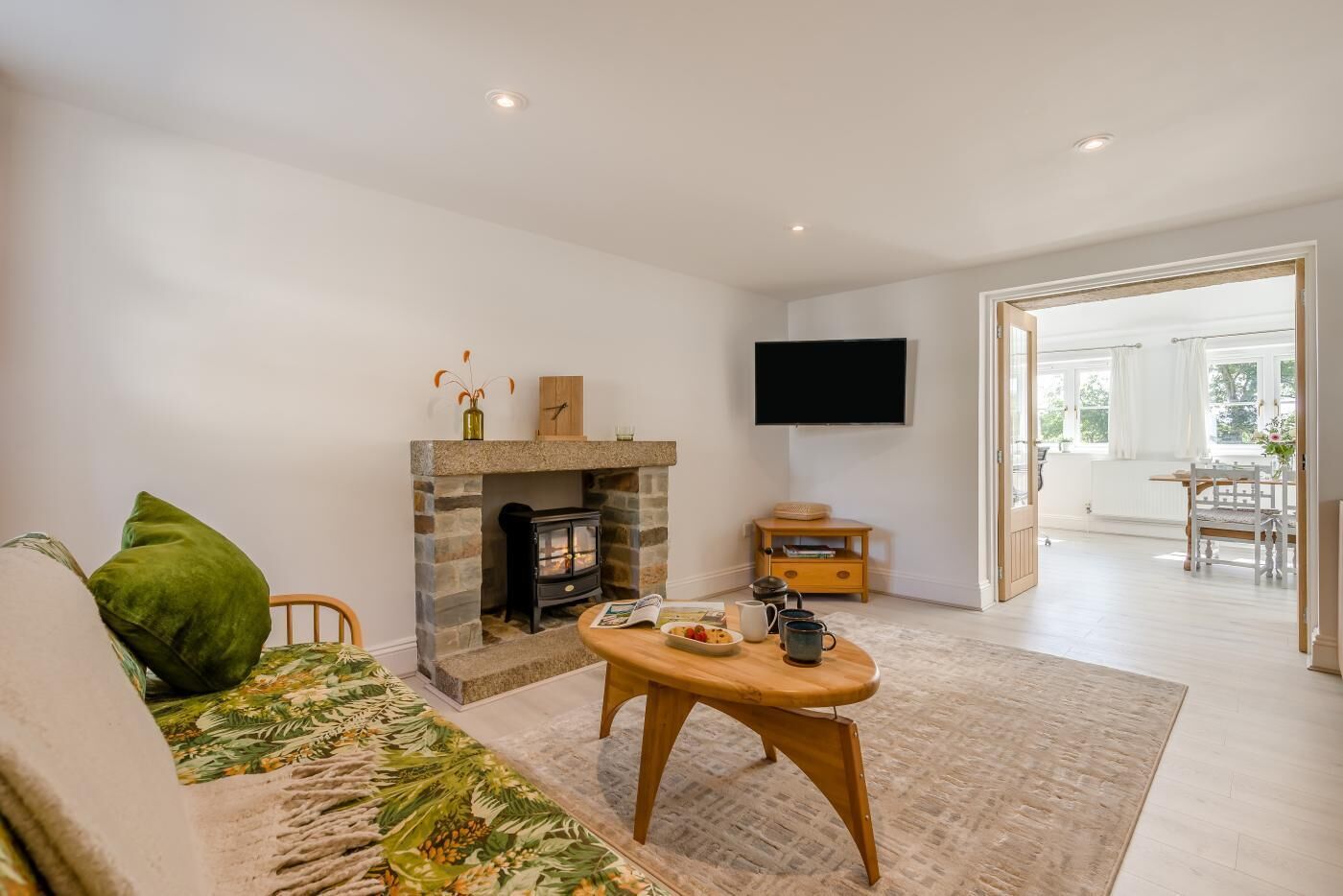 A living room with a fireplace, a flat-screen TV, a dining area, and a view of the outdoors.