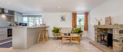 Eine moderne Küche mit einer zentralen Kochinsel, ein Essbereich mit Sofa und Couchtisch sowie ein Kamin aus Stein.