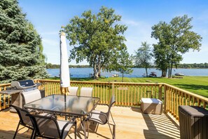 Eine Terrasse mit Glastisch und Stühlen, mit Blick auf einen See mit Booten und einer Rasenfläche.