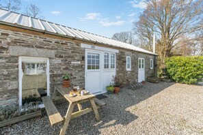A stone building with a metal roof, a wooden table with outdoor seating, and potted plants. - 1 Bed in Summercourt (oc-o36891) (Summercourt)