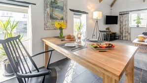 Een eetgedeelte met een houten tafel, stoelen, een bloevas en een bord eten.