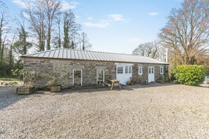 A stone building with a metal roof, a gravel driveway, and potted plants. - 1 Bed in Summercourt (oc-o36891) (Summercourt)