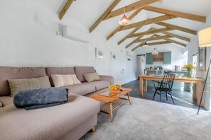 A modern living room with a sofa, a coffee table with fruit, and a dining area with a table and chairs. - 1 Bed in Summercourt (oc-o36891) (Summercourt)