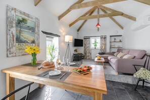 A cozy living room with a wooden dining table, a sofa, and a TV mounted on the wall. - 1 Bed in Summercourt (oc-o36891) (Summercourt)