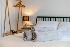 A neatly made bed with rolled towels, a bedside table with a lamp, and a wooden hanger stand. - 1 Bed in Summercourt (oc-o36891) (Summercourt)
