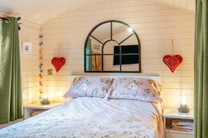 Ein Schlafzimmer mit einem Bett, einem Spiegel, herzförmigen Dekorationen und einer Girlande bunter Kugeln.