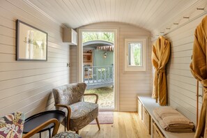 Ein gemütliches Zimmer mit einer Holzbank, einem Sessel, einem kleinen Tisch und einer Tür, die auf einen Außenbereich mit einem Balkon führt.