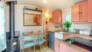 A compact kitchen with a wood-burning stove, a dining area with chairs, and pink cabinets. - 1 Bed in Shipley (oc-s34110) (Shipley)