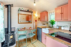 Eine kompakte Küche mit Holzofen, einem Essbereich mit Stühlen und rosa Schränken.