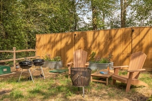An outdoor seating area with Adirondack chairs, a table, and a barbecue grill.