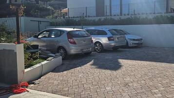 A parking area with two cars parked in a row, a paved walkway, and a building with a fence in the background.