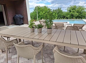 An outdoor patio with a dining table, chairs, potted plants, and a pool in the background. - Two Bedroom Villa with Swimming Pool (Jastrebarsko)