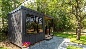 A modern outdoor structure with a large window, a wooden deck, and a potted plant. - 1 Bed in West Yelland (oc-o45728) (Braunton)