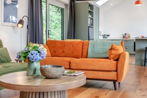 A modern living room with a sofa, a round wooden table, and a vase of flowers. - 1 Bed in Eggesford (oc-l45452) (Wembworthy)