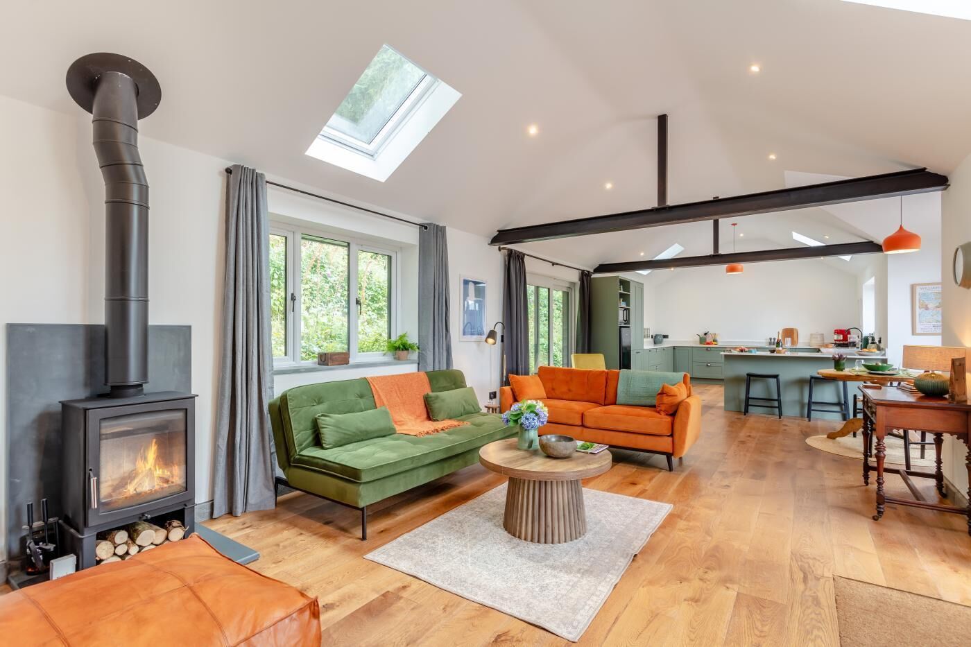 Ein modernes Wohnzimmer mit Kamin, grünen und orangefarbenen Sofas, einem Couchtisch und einer Küche im Hintergrund.