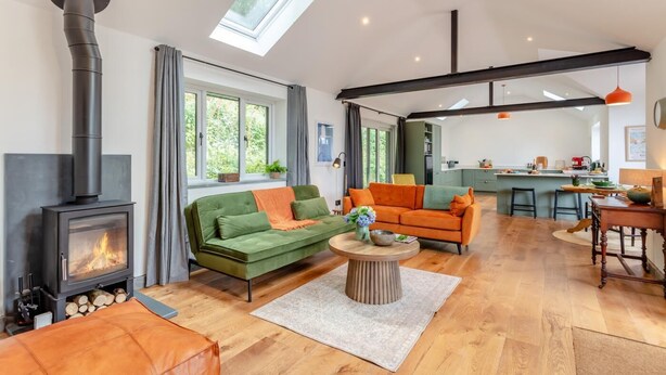 Ein modernes Wohnzimmer mit Kamin, grünen und orangefarbenen Sofas, einem Couchtisch und einer Küche im Hintergrund.