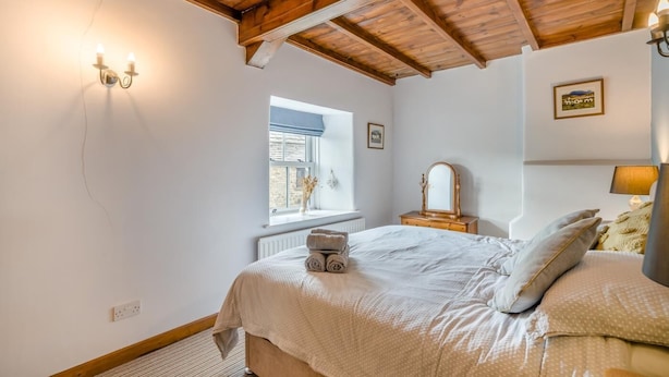 A bedroom with a wooden ceiling, a bed with rolled towels, a dresser with a mirror, and a window with a view. - 2 Bed in Appersett (oc-d45772) (Appersett)