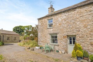 A stone house with a paved driveway, a small patio with a chair, and potted plants. - 2 Bed in Appersett (oc-d45772) (Appersett)