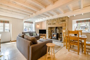 A cozy living room with a stone fireplace, a sofa, a TV, and a dining area with wooden furniture.
