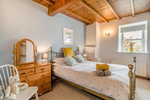 A bedroom with a bed, a dresser, a chair, a window, and a wall-mounted light fixture.